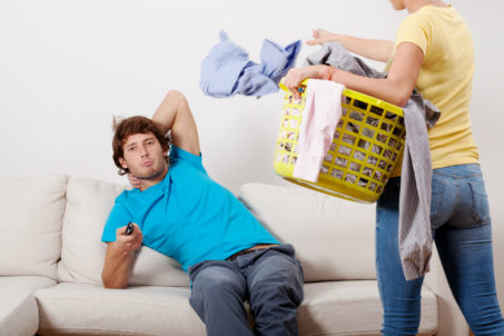 A woman with a laundry basket and a man watching tv